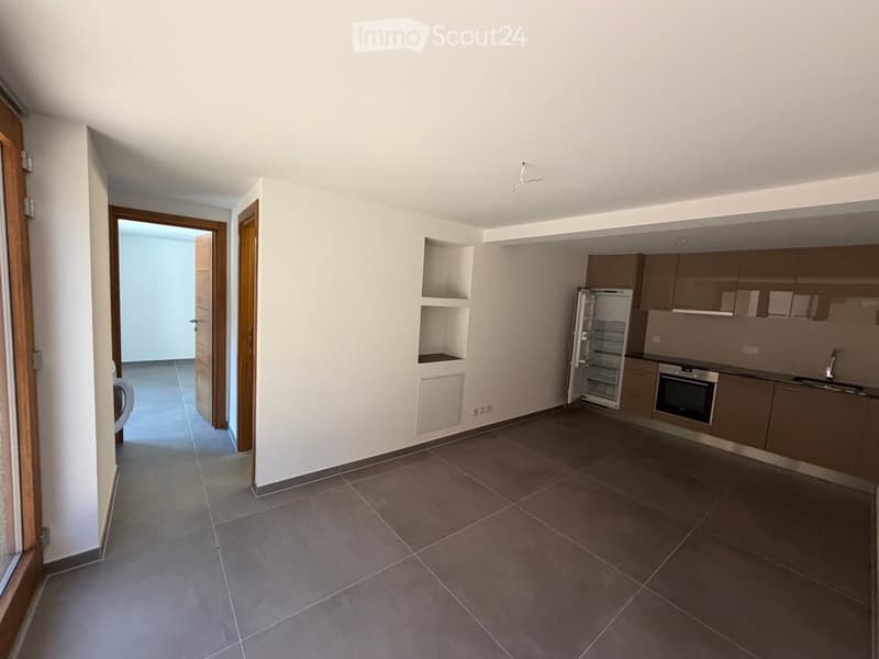 Modern kitchen with tiled floor, light-colored cabinets, stainless steel appliances, and an open doorway leading to another room.