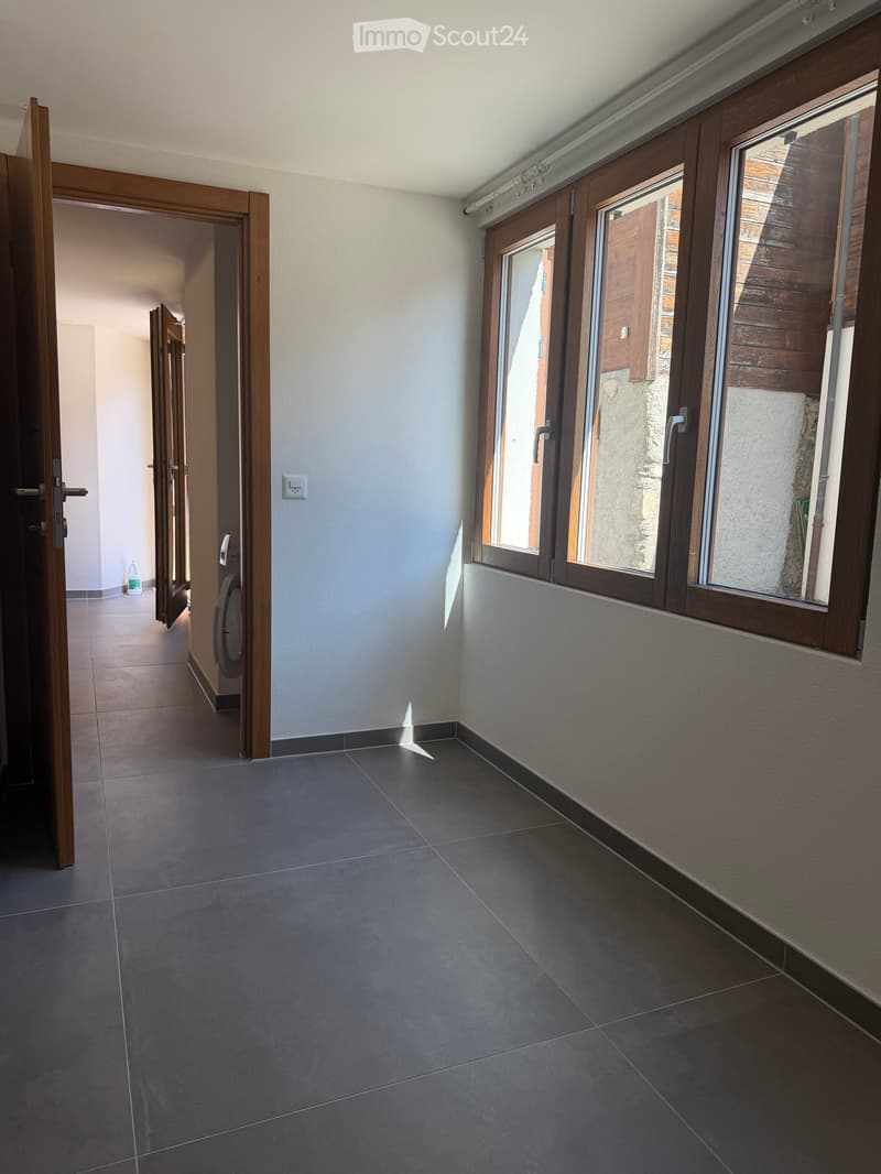 Empty room with tiled floor, large windows, and open doors leading to another area.