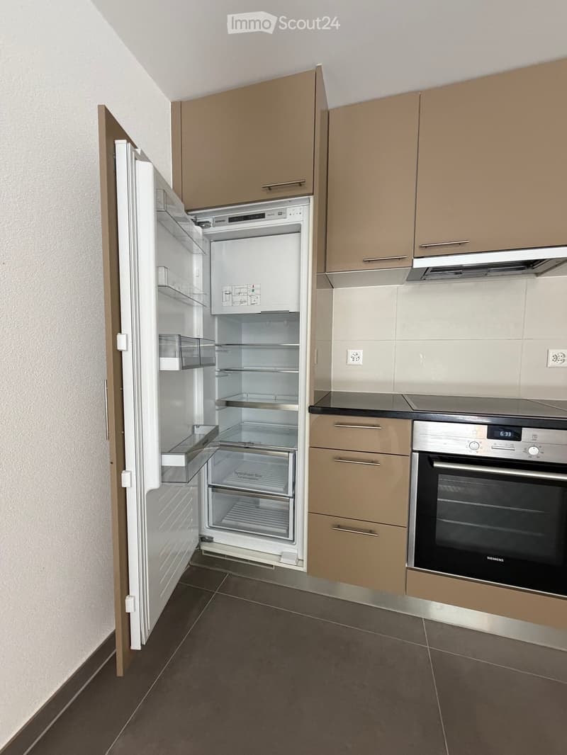 Modern kitchen with light brown cabinets, stainless steel appliances, and dark tiled flooring.