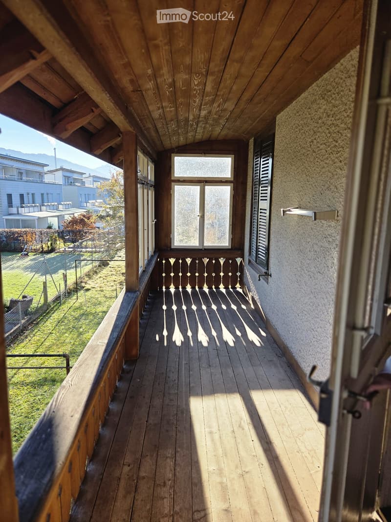 Wooden balcony with slatted railing, double doors, and wooden floorboards.