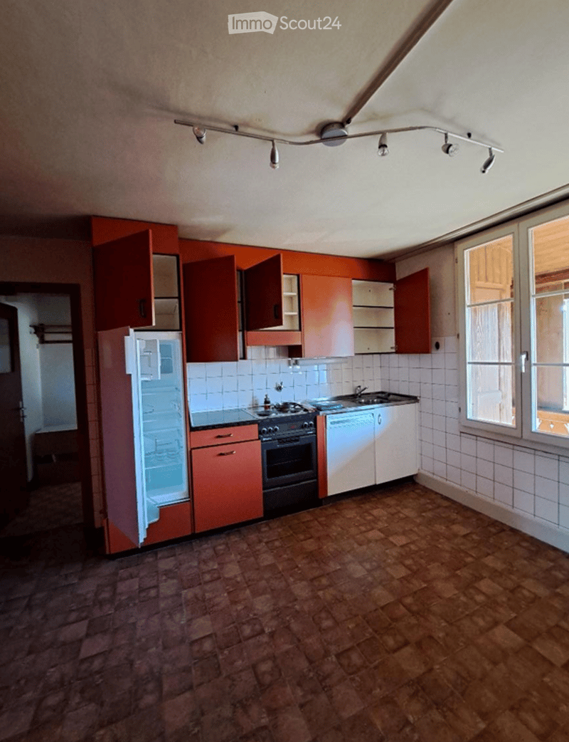 Empty kitchen with red cabinets, white tiles, and a brick floor. Features a refrigerator, oven, and sink.