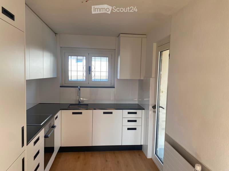 Modern kitchen with white cabinets, black countertops, a sink, and an oven. The space features wooden flooring and a window with a grid pattern.