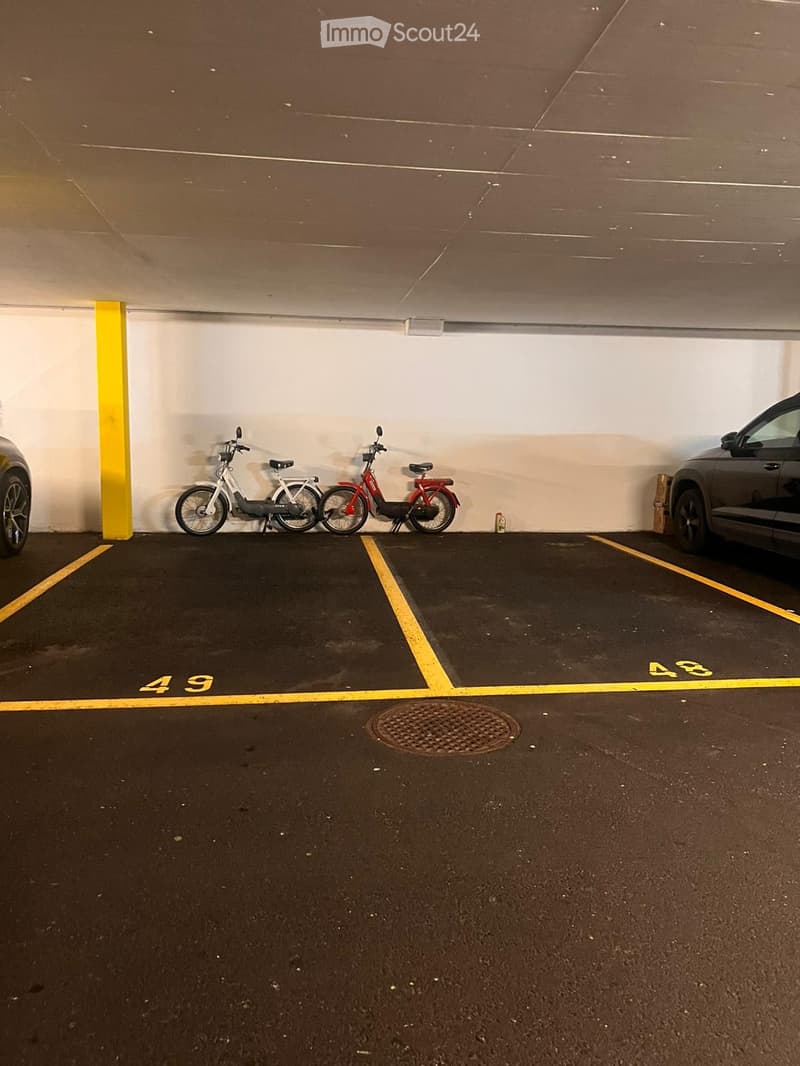 Underground parking area with marked parking spaces, bicycles, and a car partially visible.