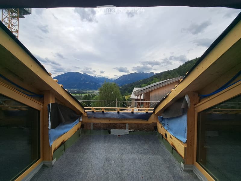 Roof terrace with wooden railings, blue insulation material, and a view of mountains and a nearby house.