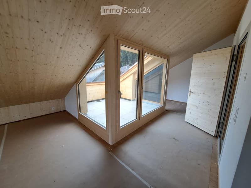 An empty attic room with wooden walls and ceiling, large windows, and a door leading to another room.