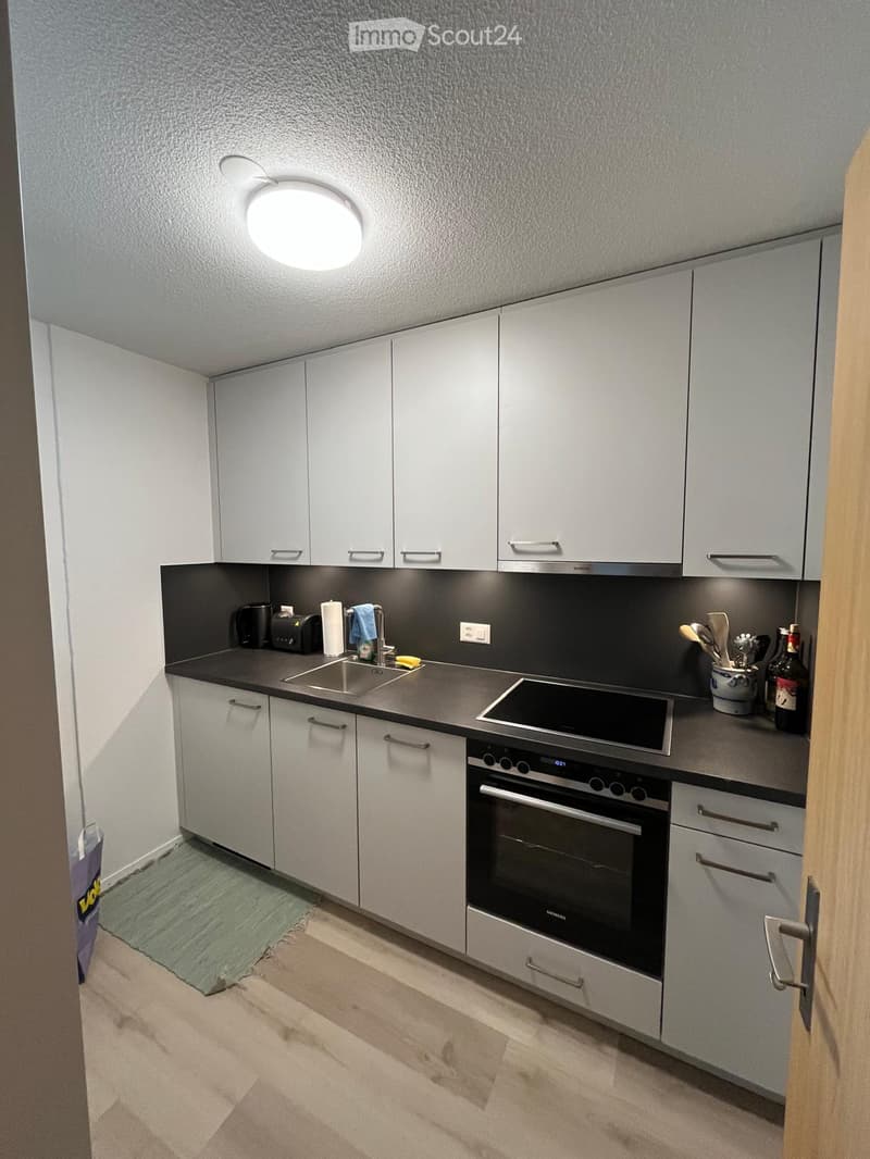Modern kitchen with white cabinets, stainless steel appliances, and a black countertop. Includes a sink, oven, stove, and various kitchen items.
