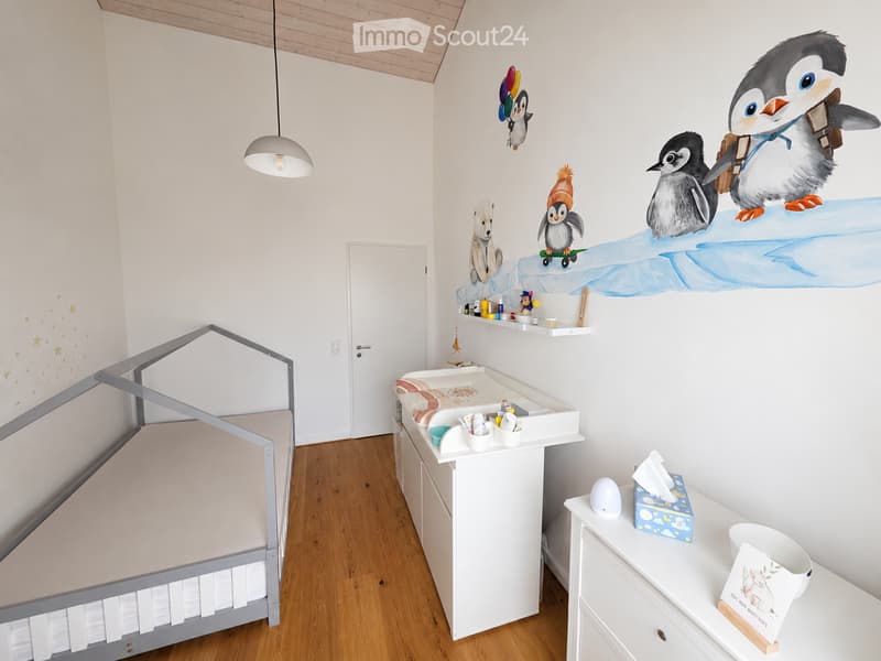 Brightly lit children's bedroom with a grey crib, changing table, shelves, and wall decals of penguins and a polar bear.