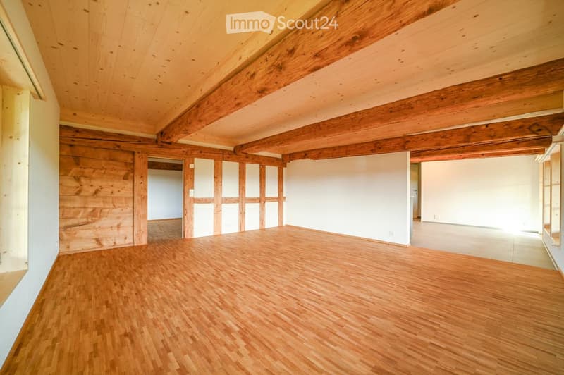 Empty room with wooden floors and exposed wooden beams on the ceiling. The walls are white, and there are no furnishings or decorations visible.