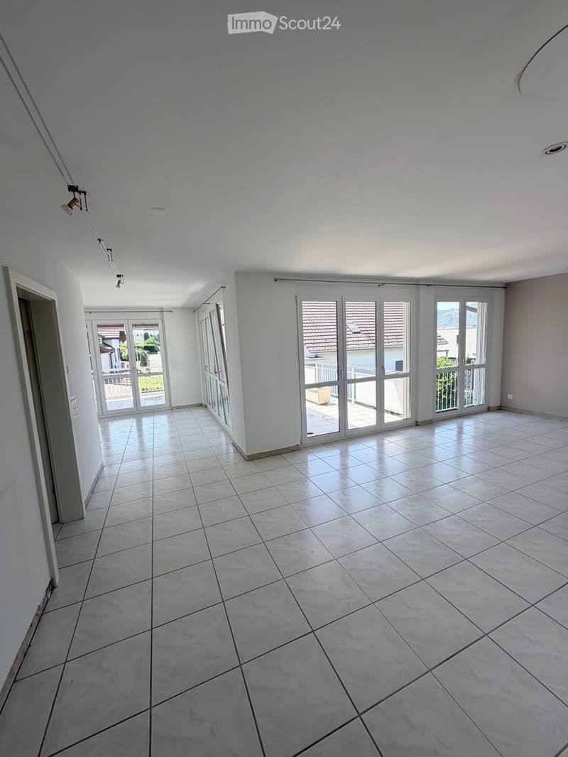 Empty room with large tiled floor, white walls, and multiple glass doors leading to a balcony or outdoor area.