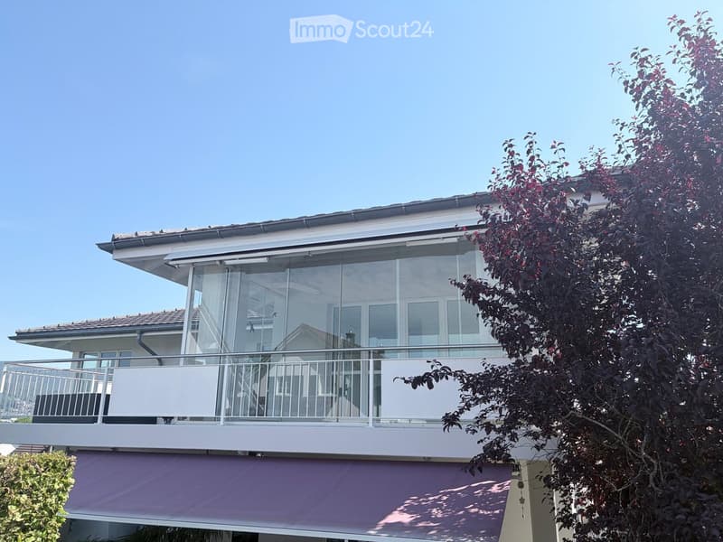 Modern two-story house with large glass windows, balcony, and purple awning on the lower level.