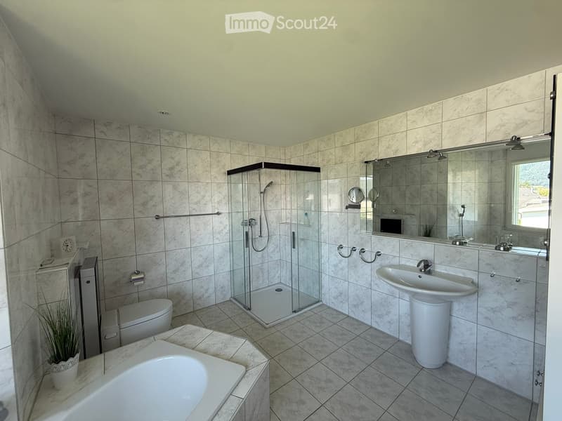 Modern bathroom with marble tiles, bathtub, toilet, sink, glass-enclosed shower, and a large mirror above the sink.