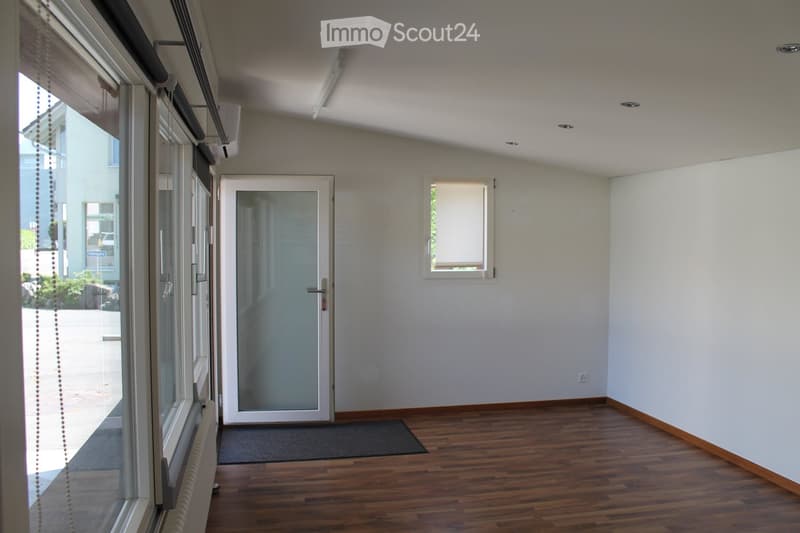 Empty room with wooden flooring, white walls, large windows, and a door leading outside. No furniture or equipment present.