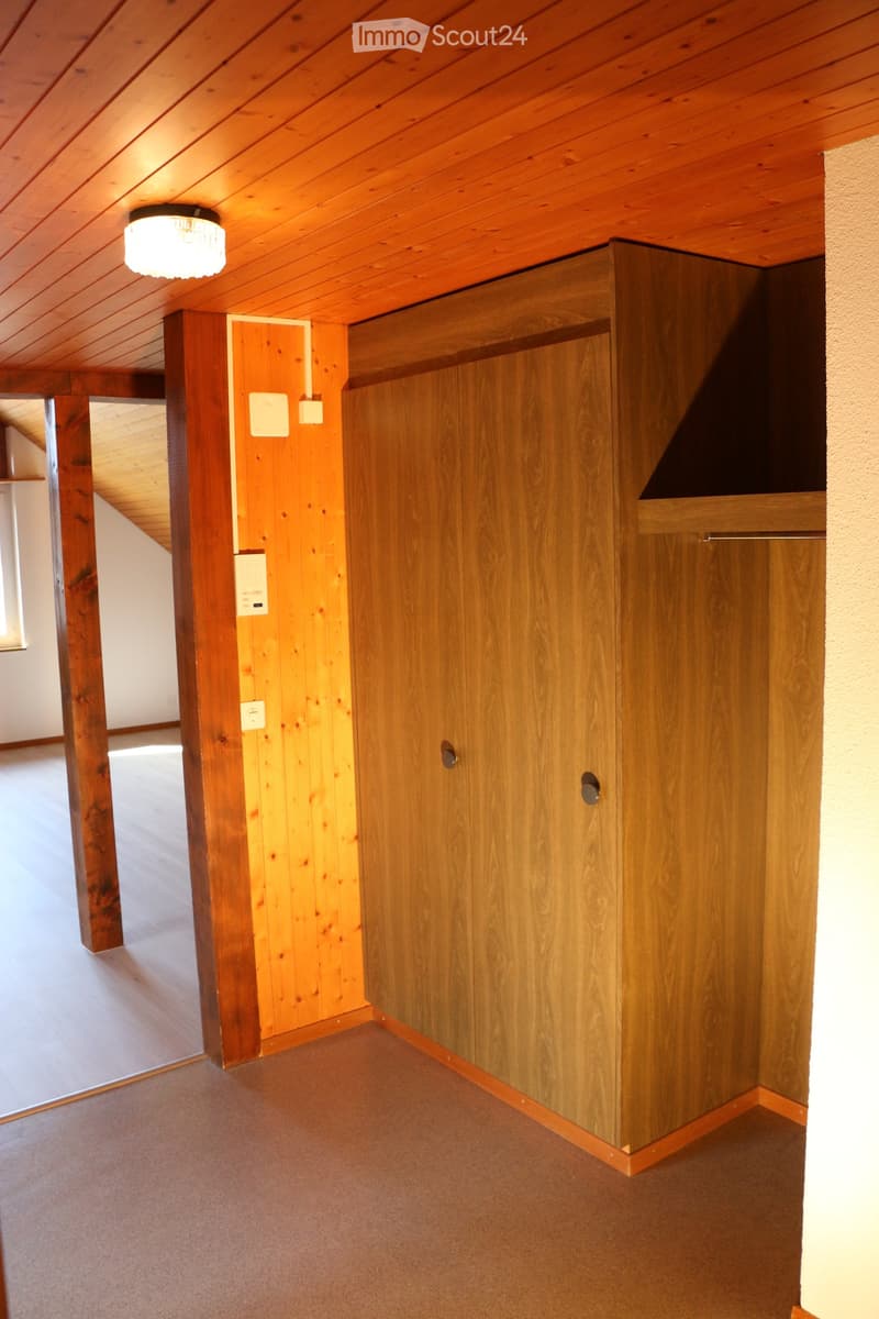 Wooden hallway with exposed beams, a closed wooden door, and a recessed light fixture on the ceiling.