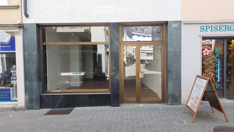 Facade of a commercial building with large glass windows and doors, including a storefront with visible interior elements like a counter and display area.