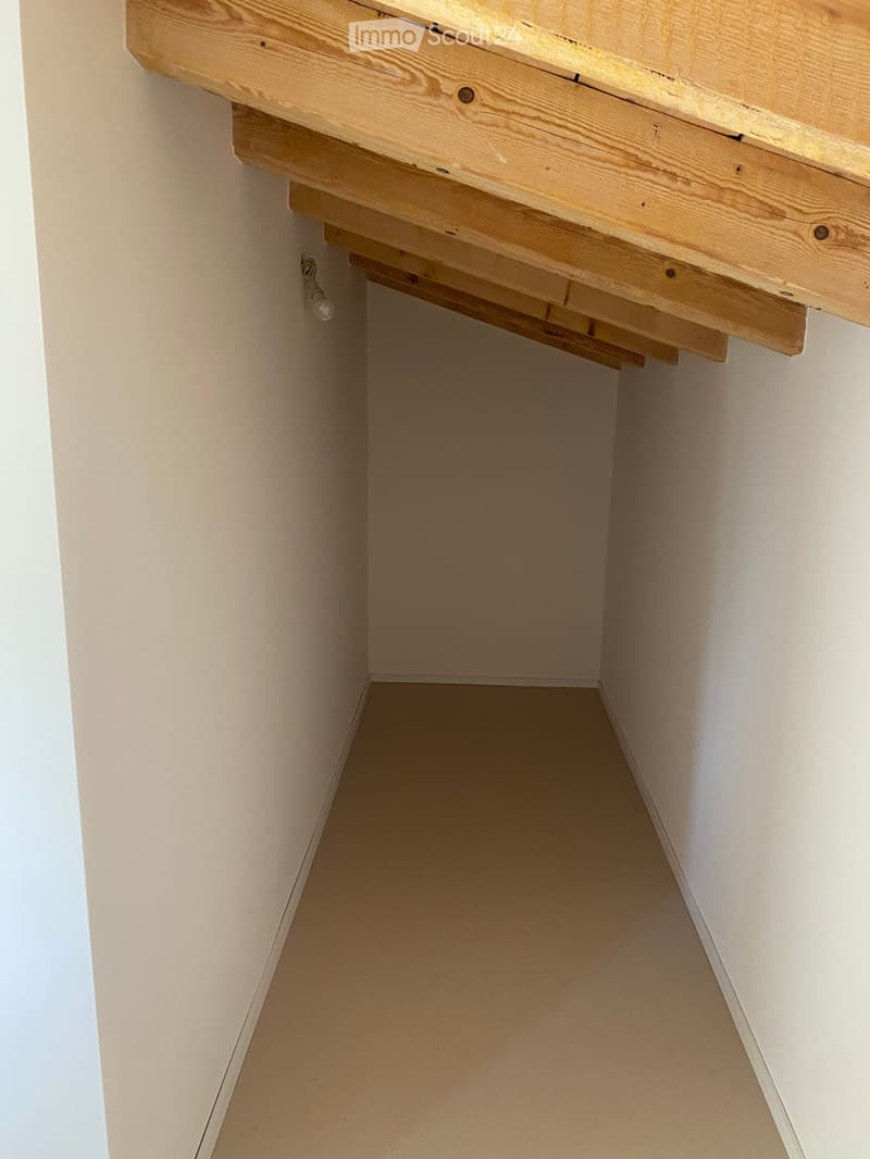 Empty closet with wooden shelves and a small light fixture on the wall.