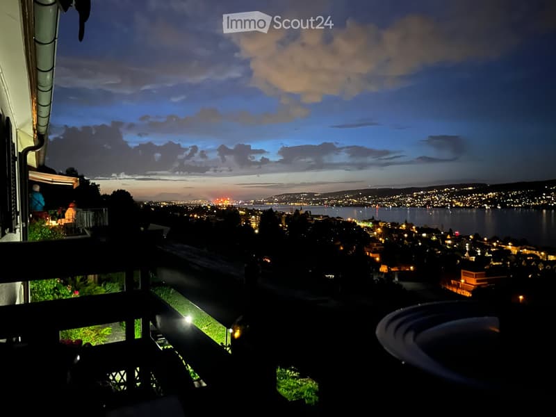 Balcony with a panoramic view of a cityscape at dusk, featuring lights and a body of water in the distance.