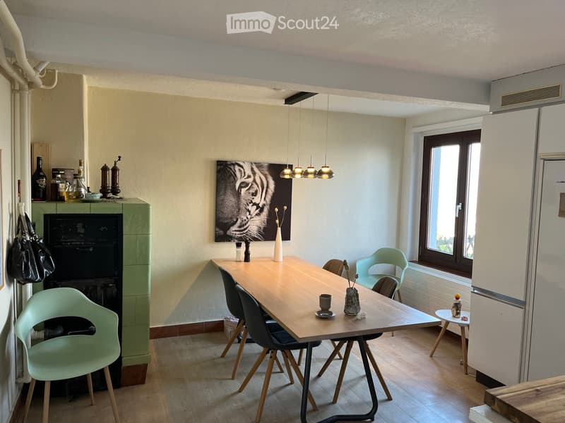 Dining area with a wooden table, chairs, a vase, a fireplace, and a large window letting in natural light.