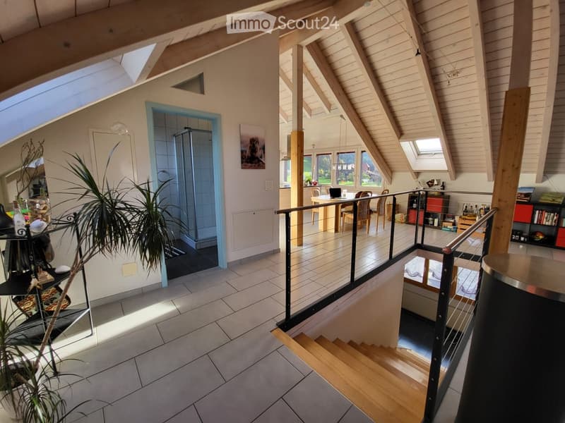 Open-plan living and dining area with wooden beams, large windows, and modern furniture including a dining table, chairs, and a laptop on the table.