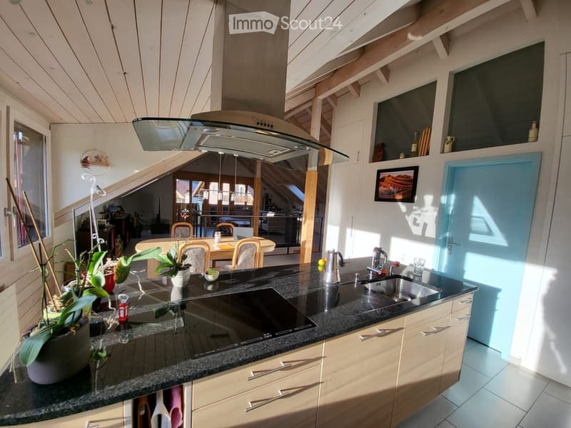 Modern kitchen with granite countertop, stainless steel sink, stove, and wooden cabinets. Features a dining area with a table and chairs, potted plants, and a framed picture on the wall.