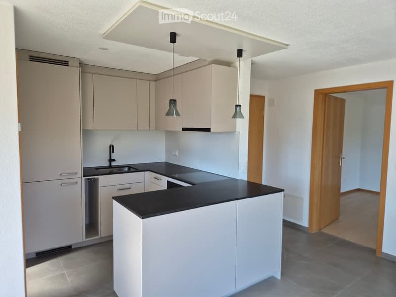 Modern kitchen with white cabinets, black countertop, and pendant lights. Features a sink with a modern faucet and a central island.