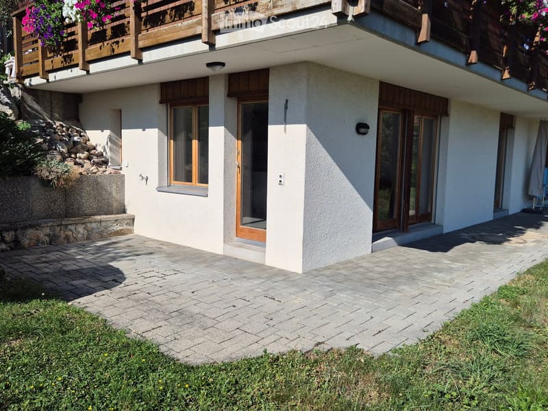Two-story house with a balcony, stone wall, and paved entrance area.