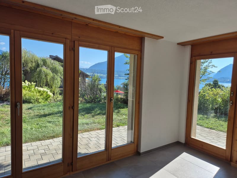 Large sliding glass doors open to a brick-paved terrace with a scenic view of a lake and mountains.