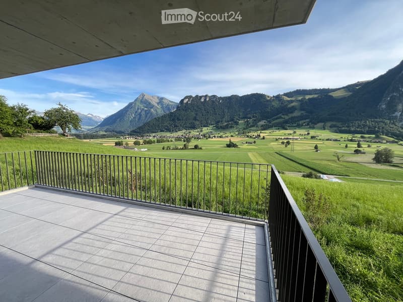 Balcony with tiled floor and metal railing, overlooking a green valley and mountain range.