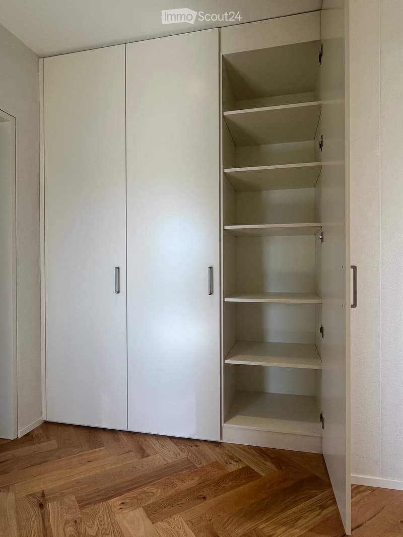 Empty room with light-colored wooden flooring and white built-in cabinets with multiple shelves.