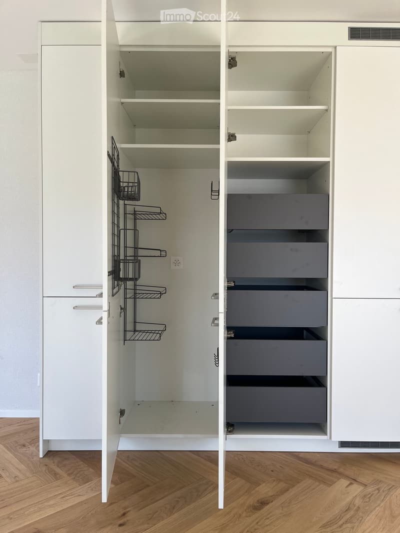Empty pantry with white cabinets, open shelves, and drawers. Wooden floor visible.