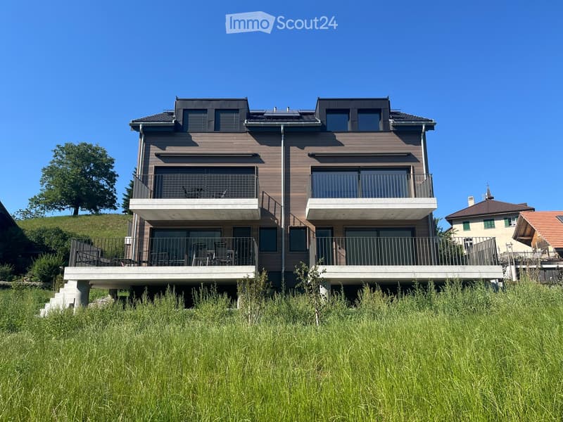Modern two-story house with wooden facade, large windows, balconies, and a raised ground floor.
