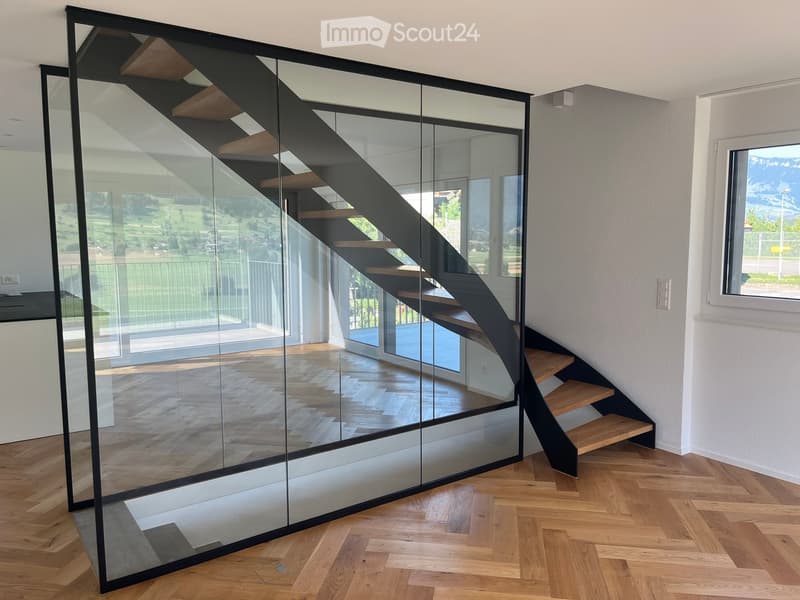 Modern hallway with wooden flooring, large mirrored wall, and a staircase with wooden steps and glass railings.