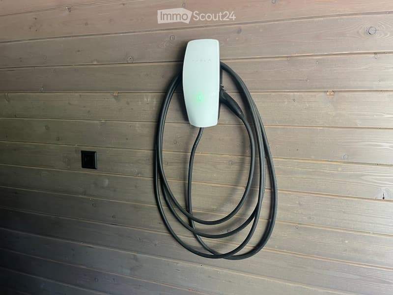 Tesla charger mounted on a wooden wall with a black cable extending downward.