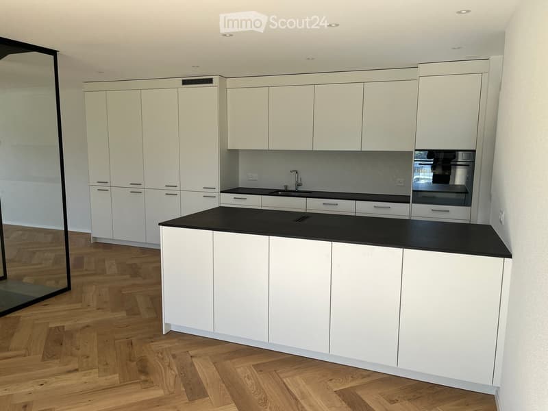 Modern kitchen with white cabinets, black countertops, and a central island. Features a sink, faucet, and built-in oven.
