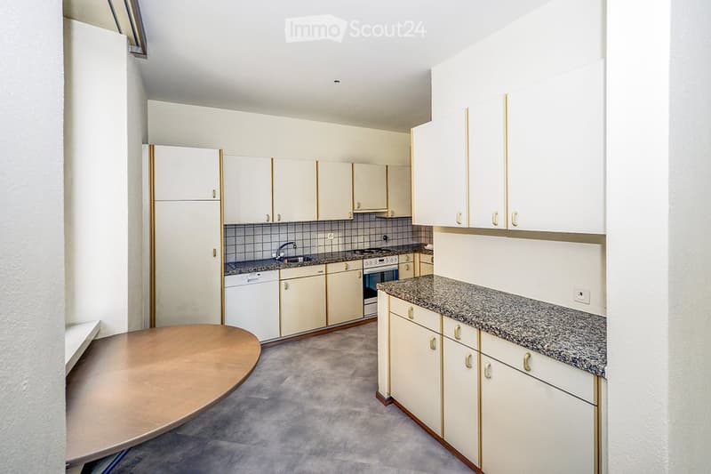 Modern kitchen with white cabinets, granite countertops, and stainless steel appliances including a fridge, oven, and dishwasher. A round wooden table is placed in the foreground.