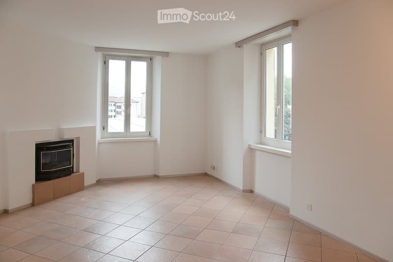 Empty room with tiled floor, white walls, two windows, and a fireplace.
