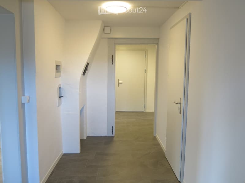 A clean, well-lit hallway with white walls, tiled flooring, and several doors leading to other rooms.