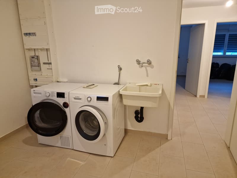 Bathroom with a washing machine, dishwasher, and a sink. The room has tiled flooring and white walls.