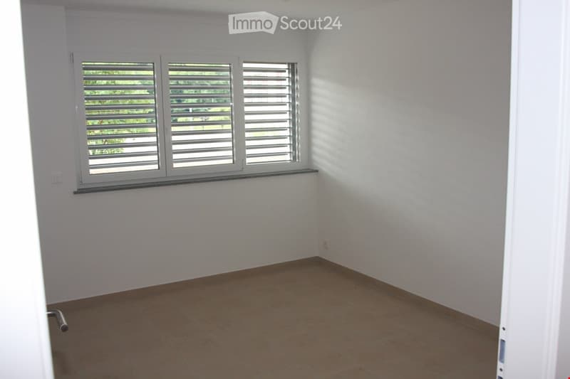 Empty room with white walls, tiled floor, and large window with blinds. No furniture or equipment present.
