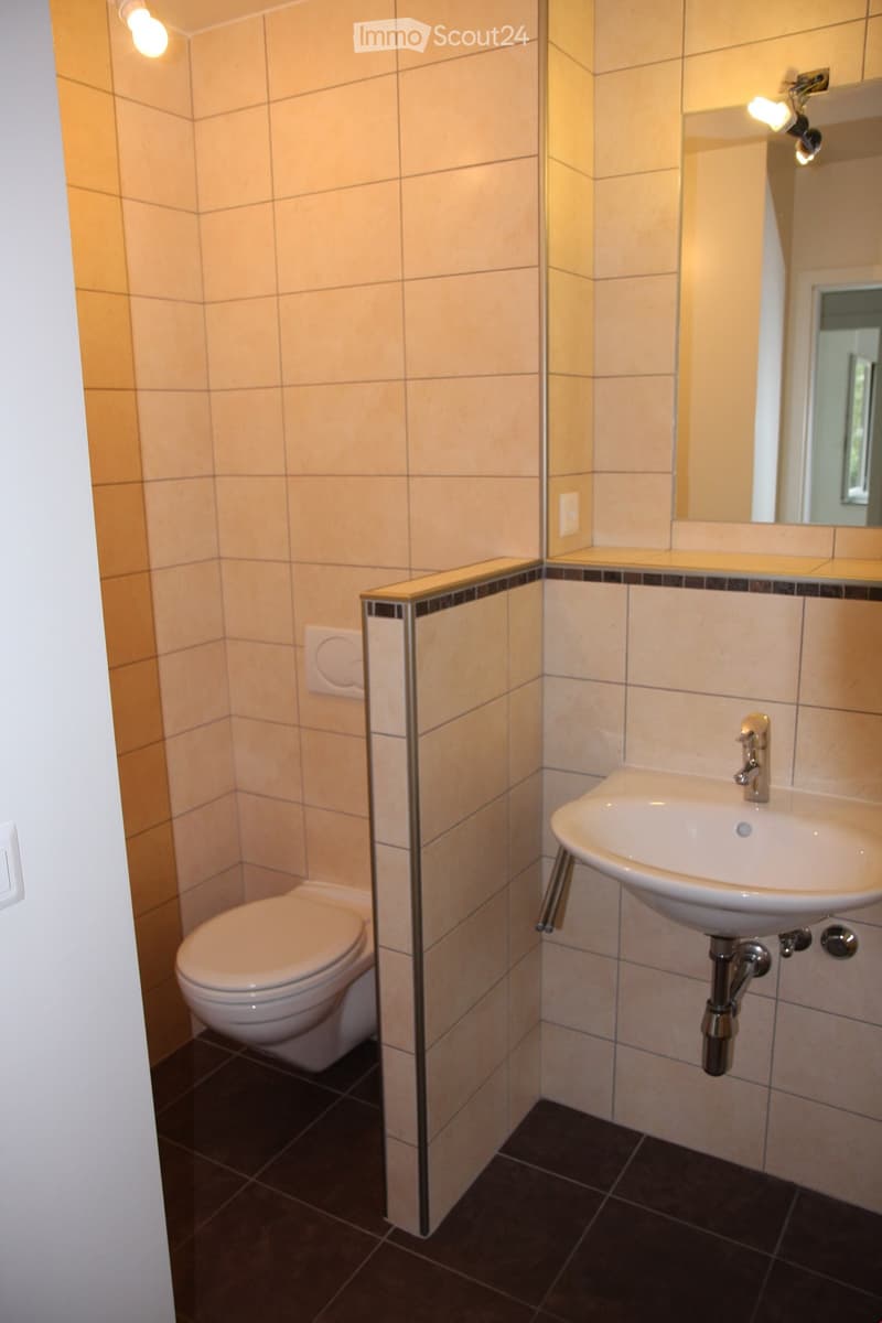 Modern bathroom with beige tiled walls, dark tiled floor, toilet, sink, and mirror.