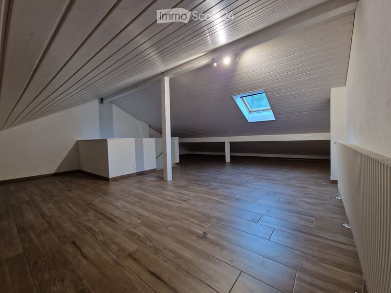 Empty attic space with wooden flooring, white walls, and a skylight window. The room features exposed wooden beams on the ceiling and built-in storage benches along one wall.
