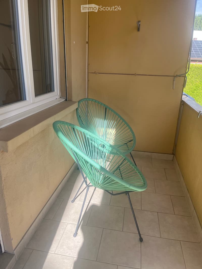 Balcony with two green wicker chairs, tiled floor, and large windows.