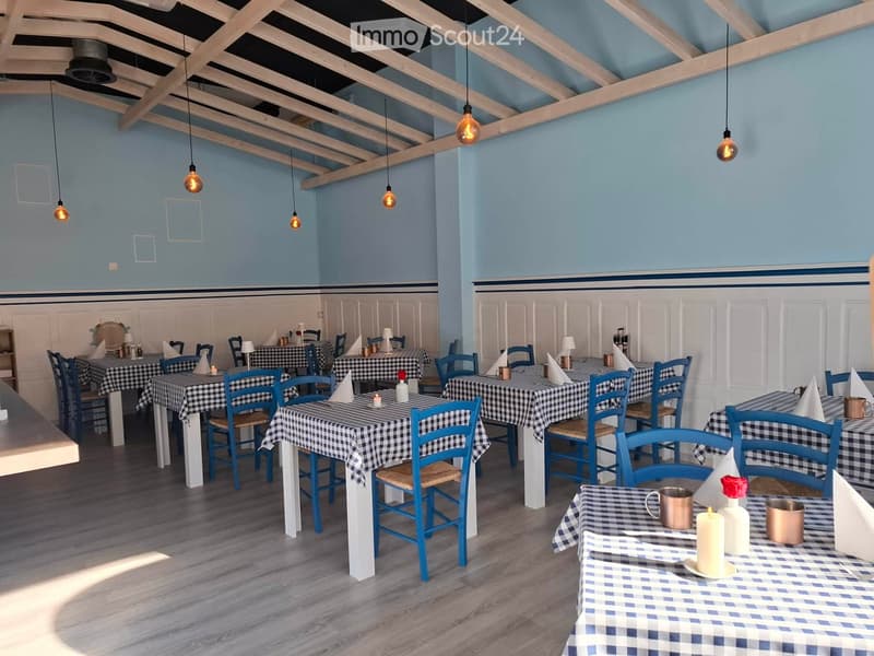 Restaurant interior with multiple tables and chairs, checkered tablecloths, and decorative items like candles and napkins.