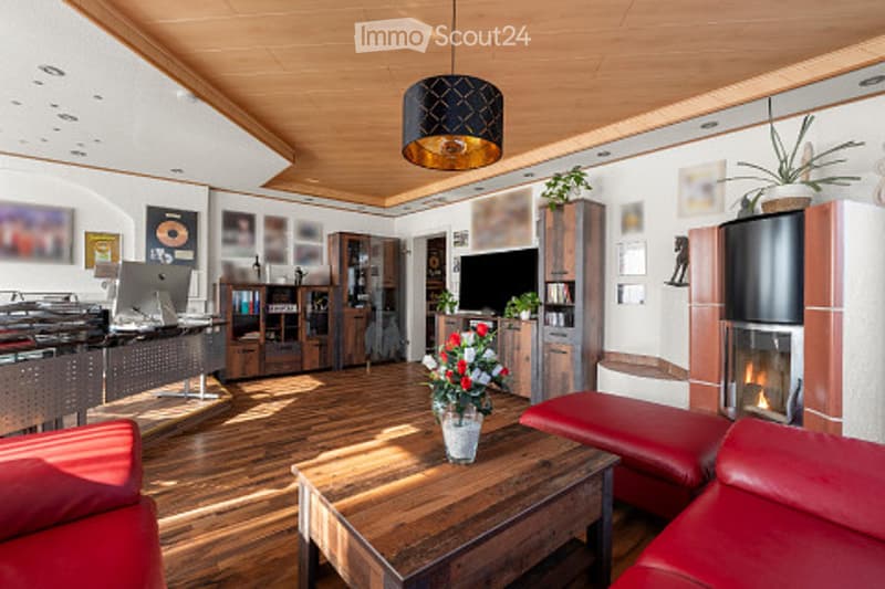 Bright living room with wooden flooring, red leather sofa, coffee table, fireplace, TV, bookshelf, and decorative flower vase.