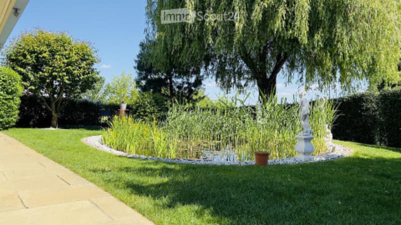 Well-maintained garden with a pond, lush greenery, a statue, and a paved pathway.