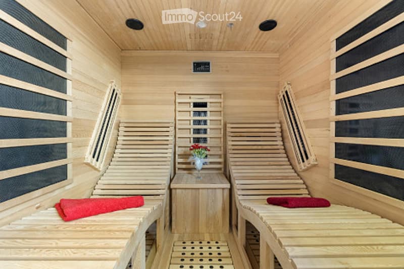 Wooden sauna interior with two wooden benches, a small table with a flower vase, and red towels placed on the benches.