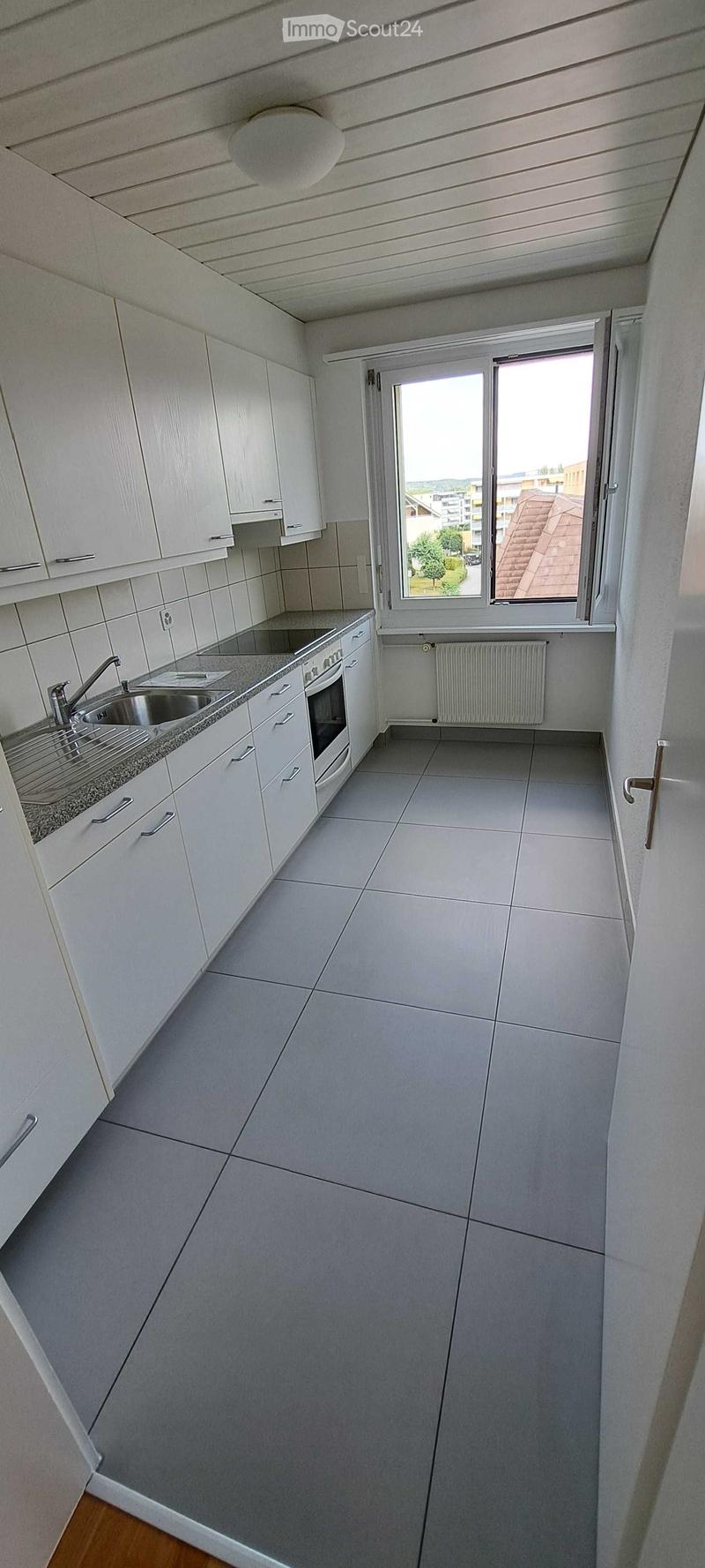 Modern kitchen with white cabinets, a sink, an oven, and a radiator. The space is clean and well-lit with a window offering a view of the outside.