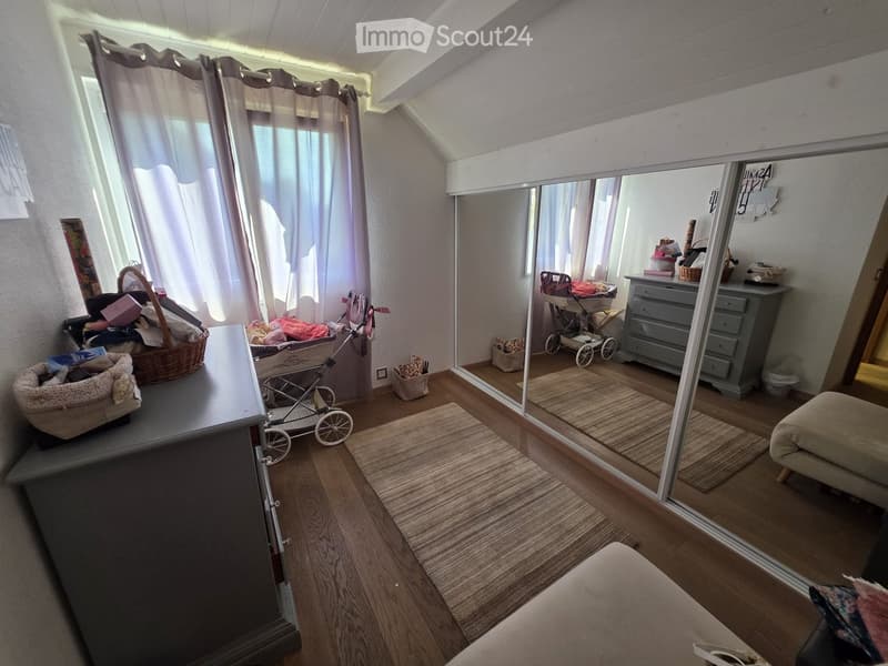 A cozy, well-lit room with wooden flooring, a large mirror, a sofa, a baby stroller, a pet bed, and a drawer unit.