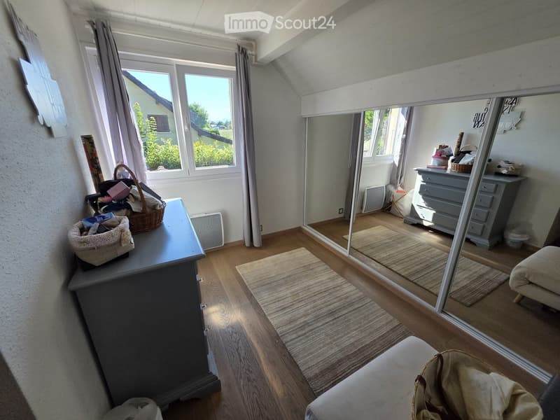 A well-lit room with wooden flooring, large windows, a sofa, a table with baskets, a mirror, and a dresser with drawers.