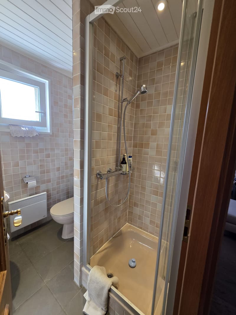 Bathroom with a toilet, bathtub, shower, towel, radiator, and a window with blinds.