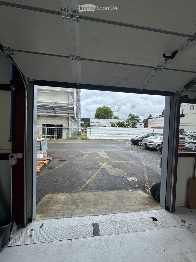 Building. View from inside a garage looking out onto a parking area with several parked cars and a construction site in the background.